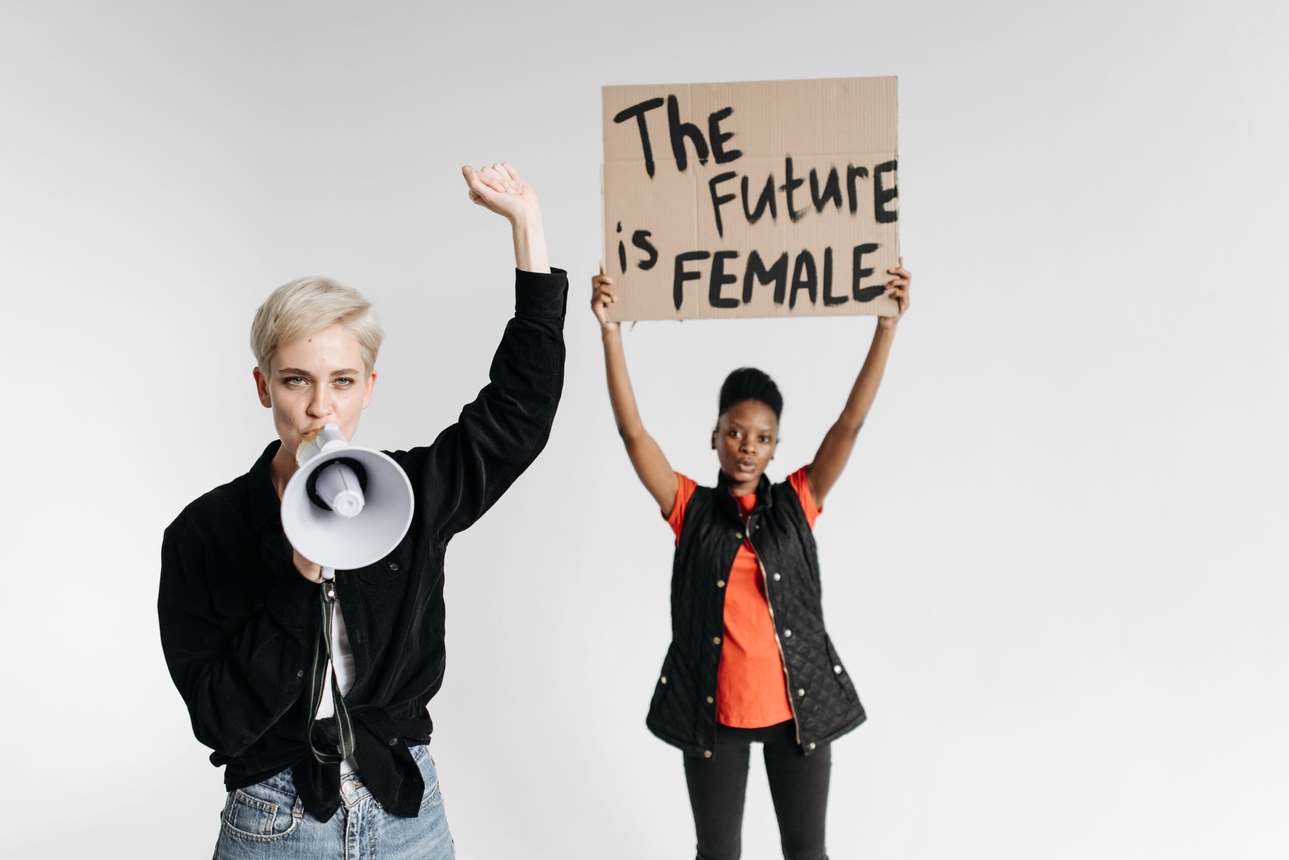 Two women advocating feminism with a sign 'The Future is Female' and a megaphone, standing indoors.